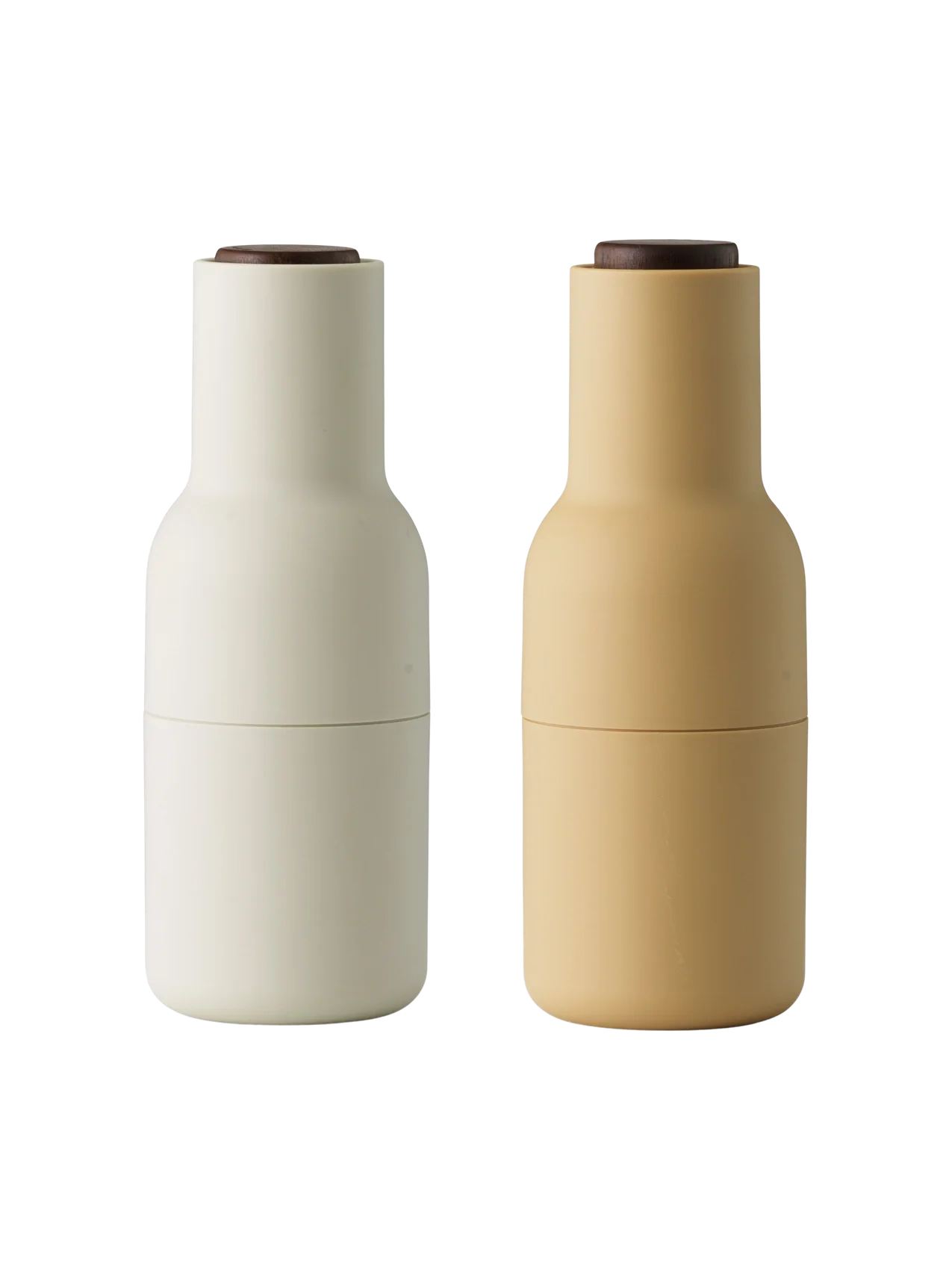 A pair of Audo Bottle Grinders, one barley and one off-white, both with dark walnut wood lids. Shot on a black background.