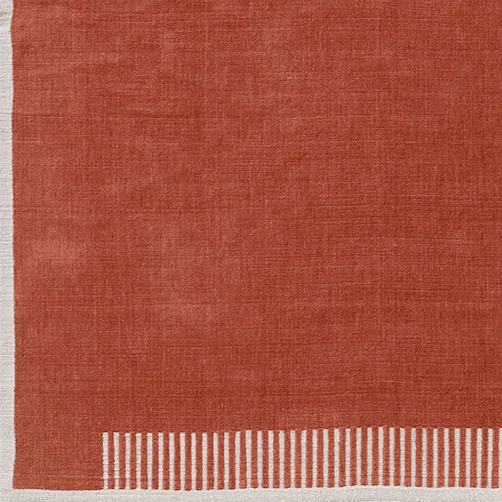 Close-up of the Duomo Rug in Terracotta Red, showing the corner with its woven texture and striped off-white border.