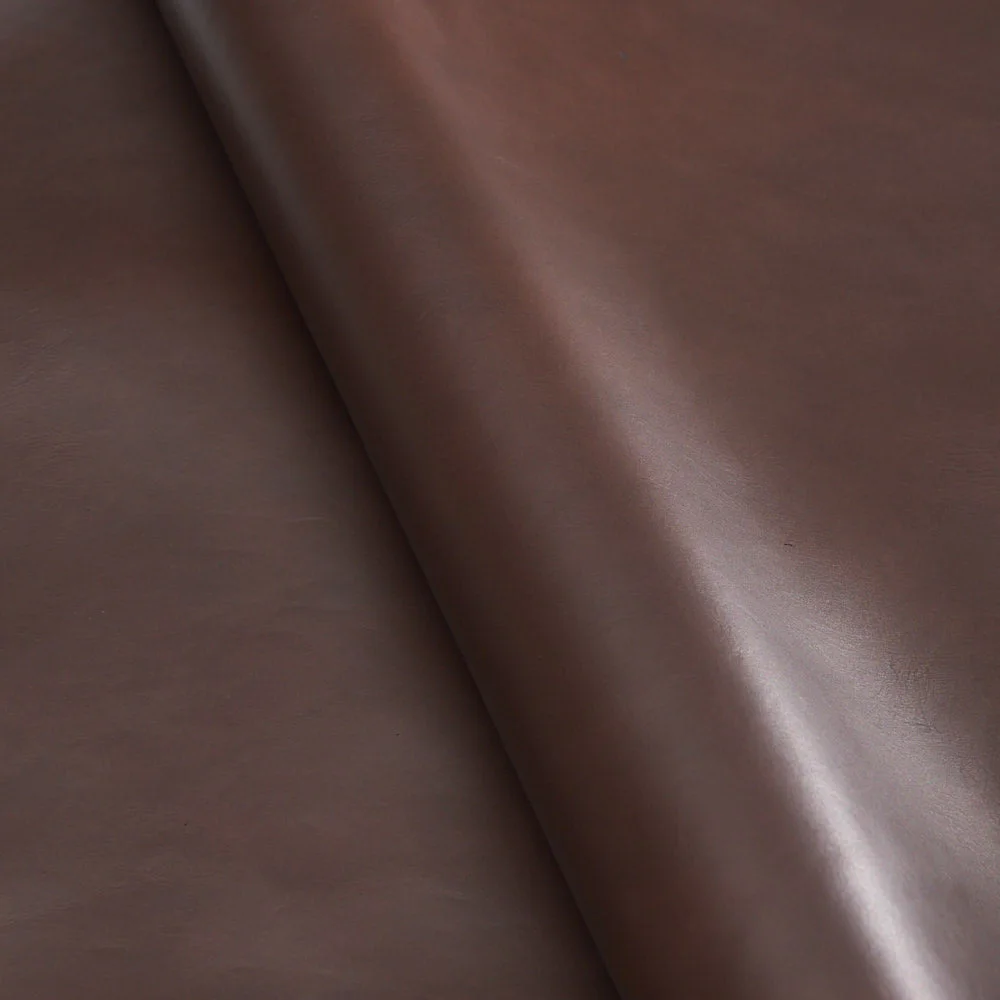 Close-up of rolled smooth dark brown leather hide with subtle sheen and soft grain texture.