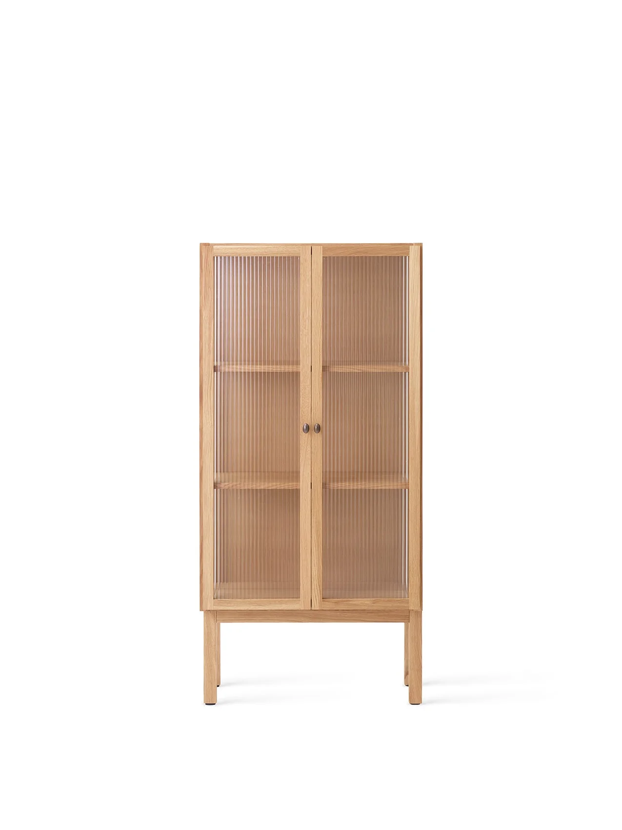Front view of the tall oak Curiosity Cabinet. It has two reeded glass doors with small brass handles and stands on four legs.
