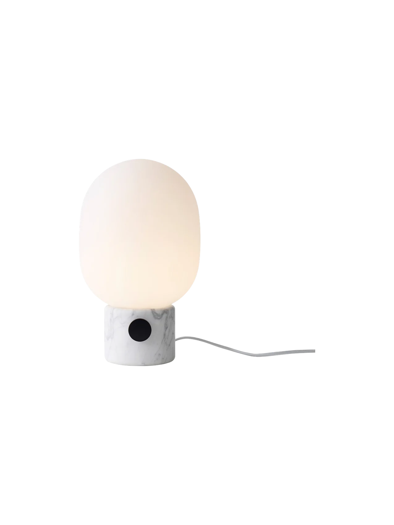 A lit JWDA Table Lamp, Large with a white Carrara marble base, black dimmer switch, and glowing opal glass shade.