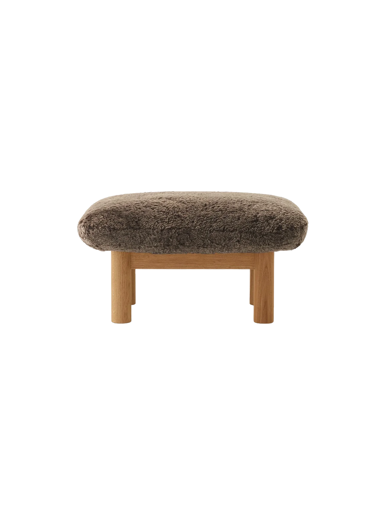 A front view of the Brasilia Ottoman, featuring a plush, brown sheepskin cushion atop a natural oak frame with robust legs.